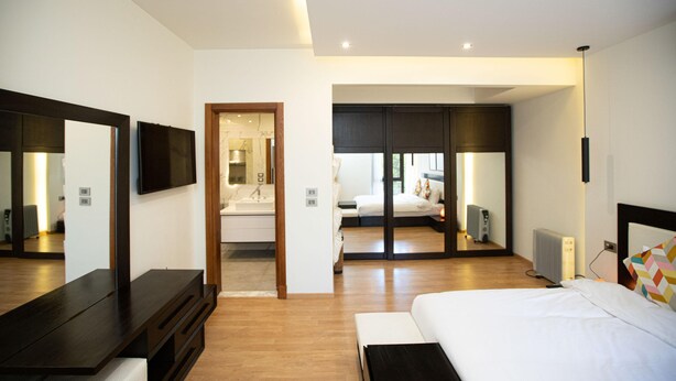 A modern hotel room with a large bed, a TV, a mirror, and a walk-in closet.