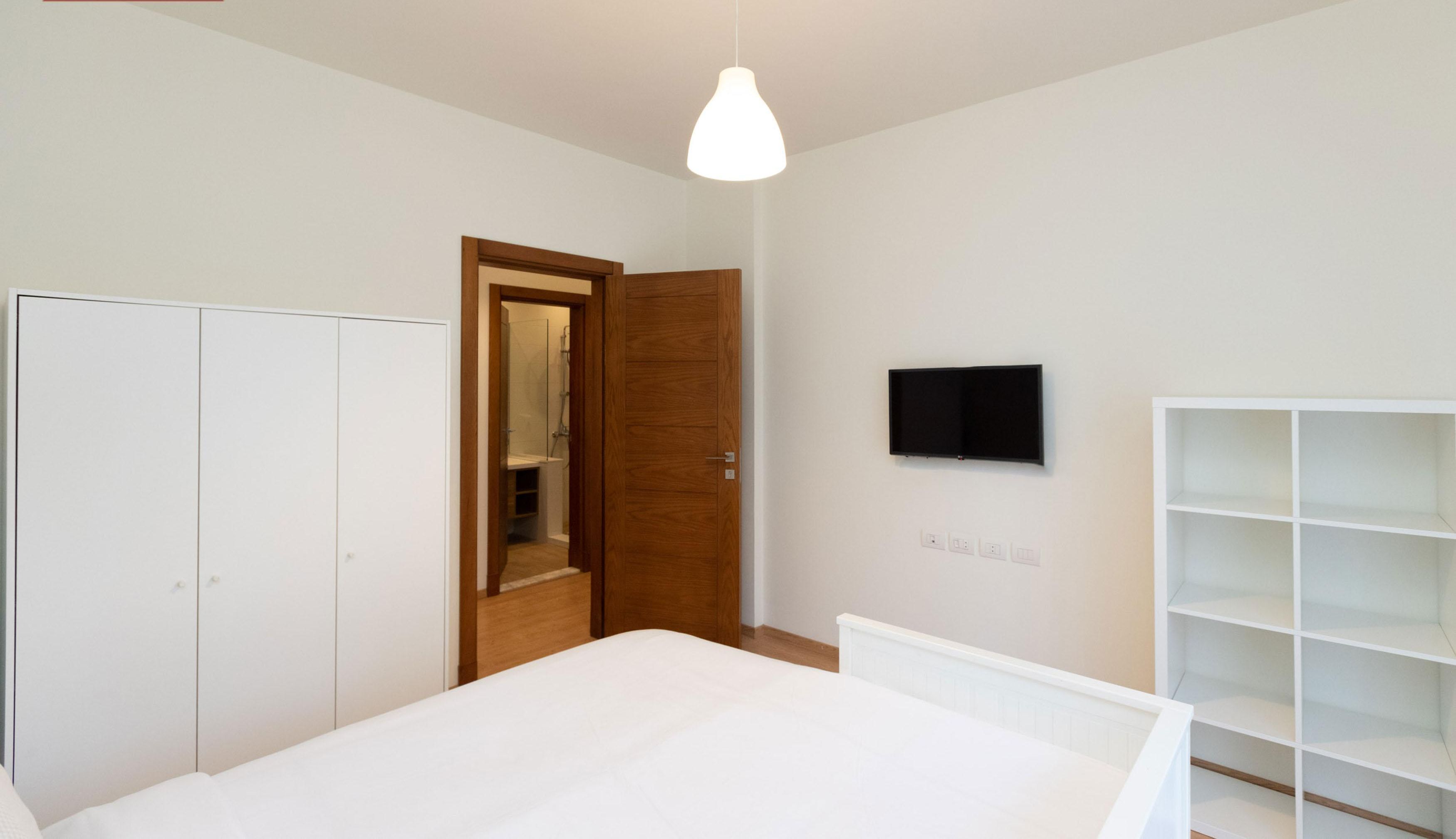 A bedroom with a bed, a wardrobe, a TV, and a bookshelf.