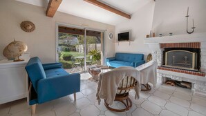 A modern living room with two blue sofas, a wooden rocking chair, a fireplace, and a large window offering a view of the outdoors. - Préfailles - House 6P - 200m from the beaches (Préfailles)