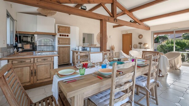 A spacious kitchen with wooden cabinets, a dining area with a wooden table and chairs, and a large window providing a view of the outdoors. - Préfailles - House 6P - 200m from the beaches (Préfailles)