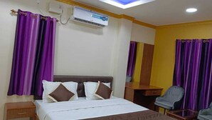 Habitación de hotel con cama, escritorio, silla, cortinas moradas y aire acondicionado.