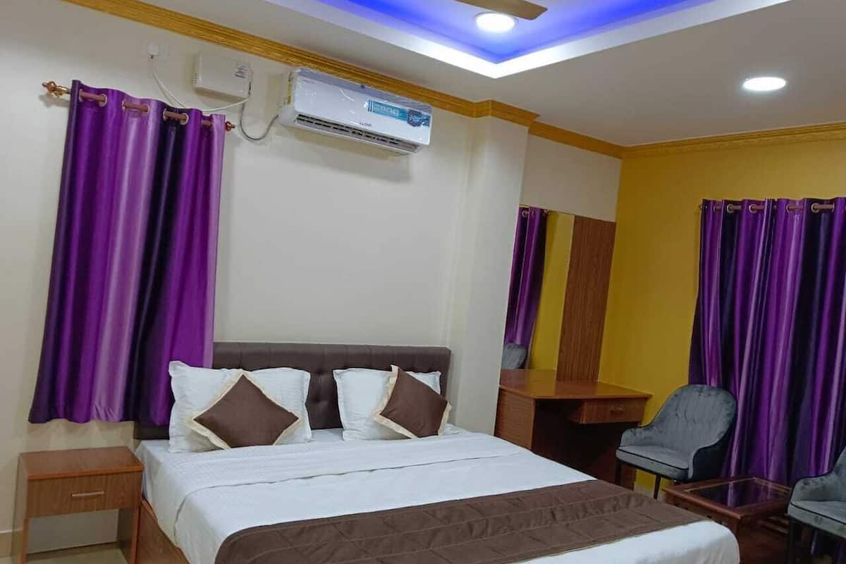 A hotel room with a bed, a desk, a chair, purple curtains, and an air conditioning unit.