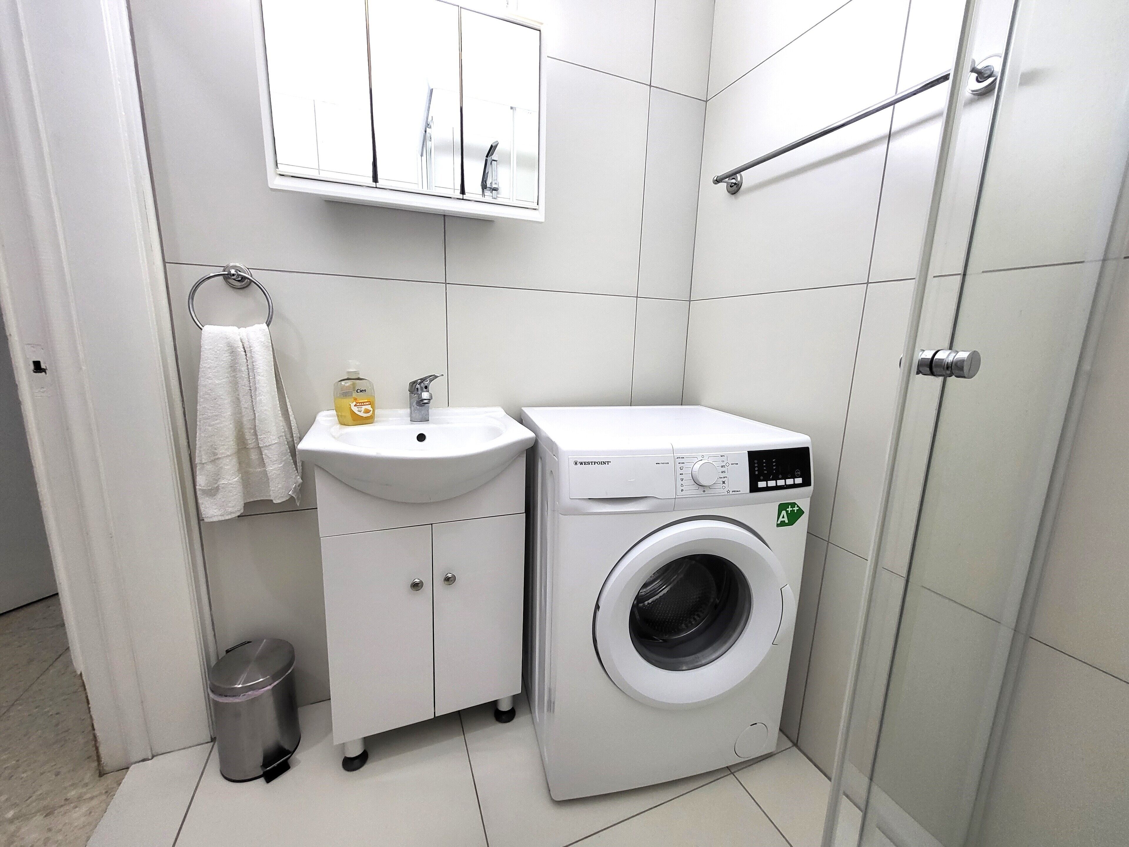Een compacte badkamer met een wit wastafel, een Westpoint wasmachine en een klein prullenbakje.