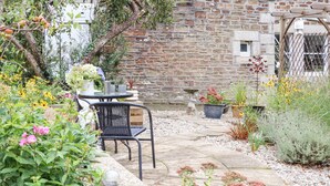 Un bâtiment en pierre doté d’un patio avec jardin, comprenant une table, des chaises et des plantes en pot.