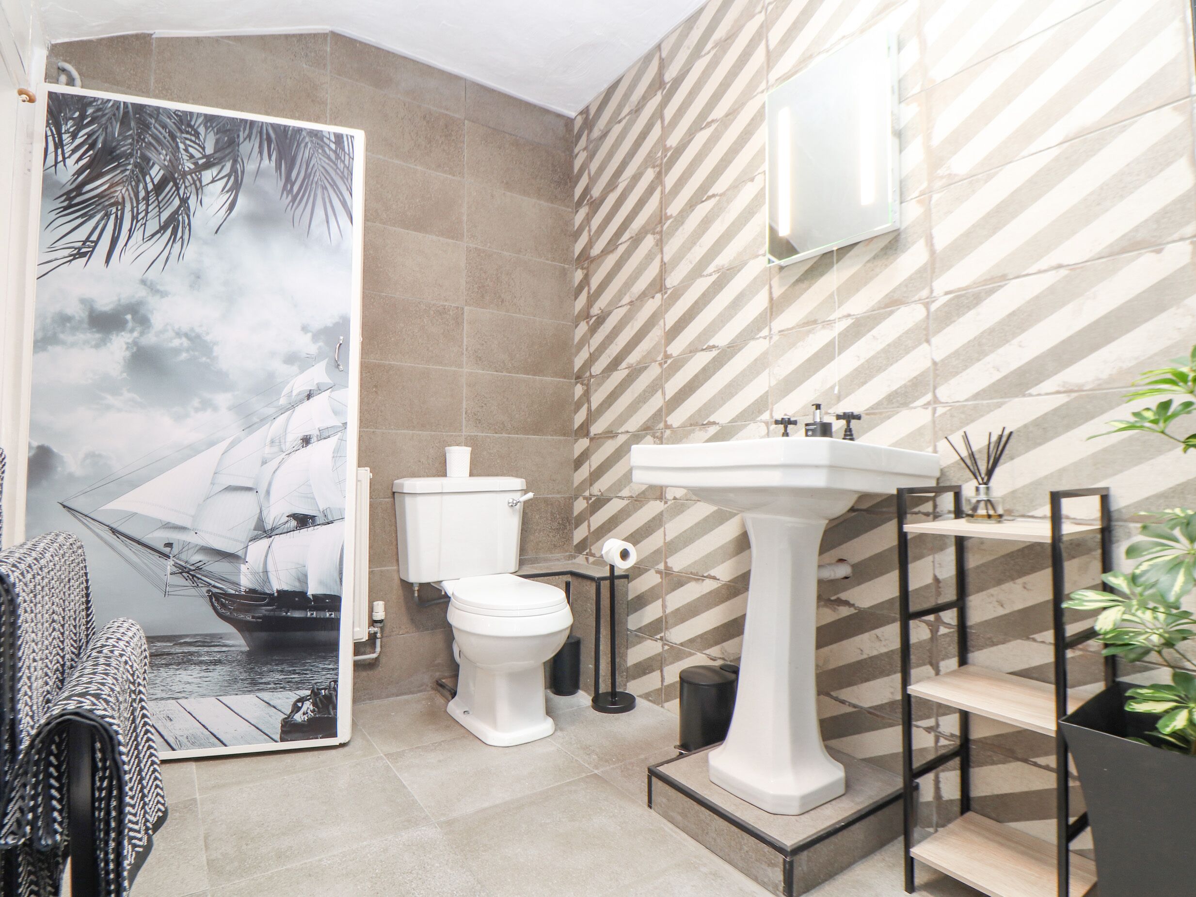 A bathroom with a large poster of a sailing ship, a white sink, and a toilet.