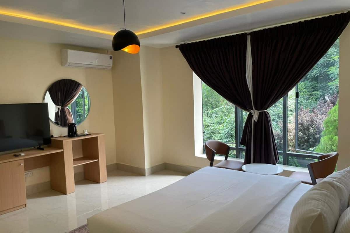 Une chambre d’hôtel moderne, dotée d’un grand lit, d’une télévision, d’un bureau et offrant une vue sur la verdure par la fenêtre.
