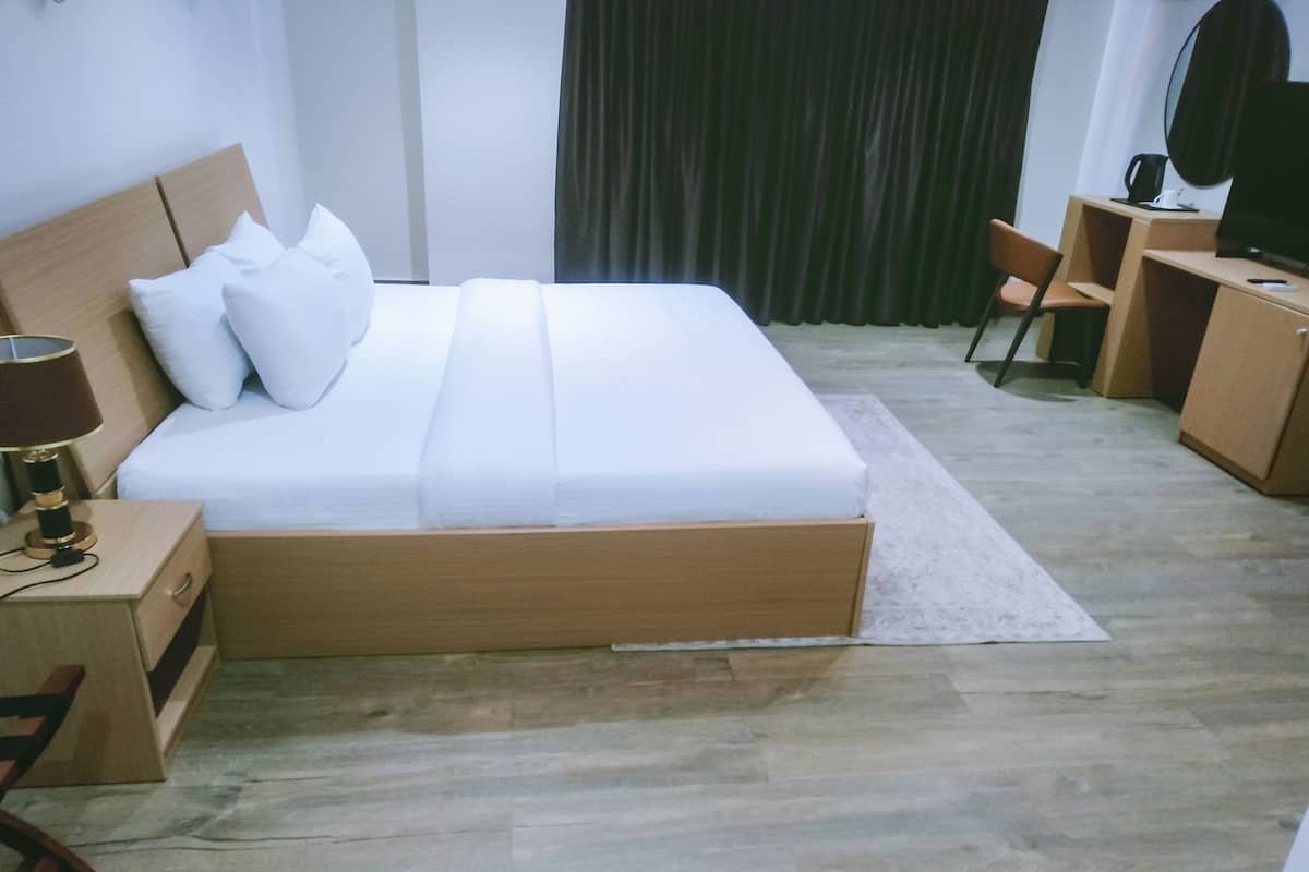 Une chambre d’hôtel bien rangée, avec un lit, une table de chevet, une lampe et un bureau avec une chaise.