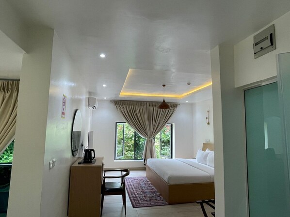 Une chambre d’hôtel comprenant un lit, un bureau avec une chaise, une machine à café, une télévision et une fenêtre avec des rideaux.