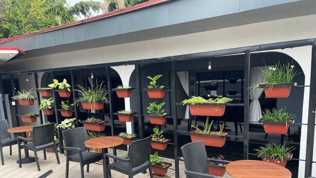 An outdoor seating area with multiple tables and chairs, surrounded by potted plants on shelves. - The Address Hotel (Abuja)