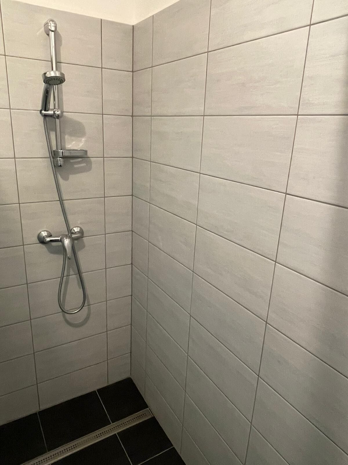Ducha en esquina con cabezal de ducha de mano y grifo empotrado.