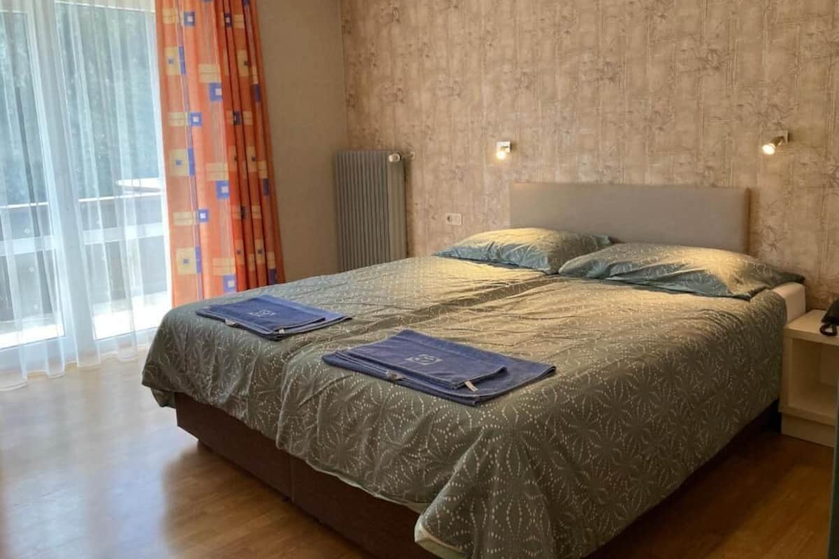 A bedroom with a large bed, a bedside table, a radiator, and a window with curtains.