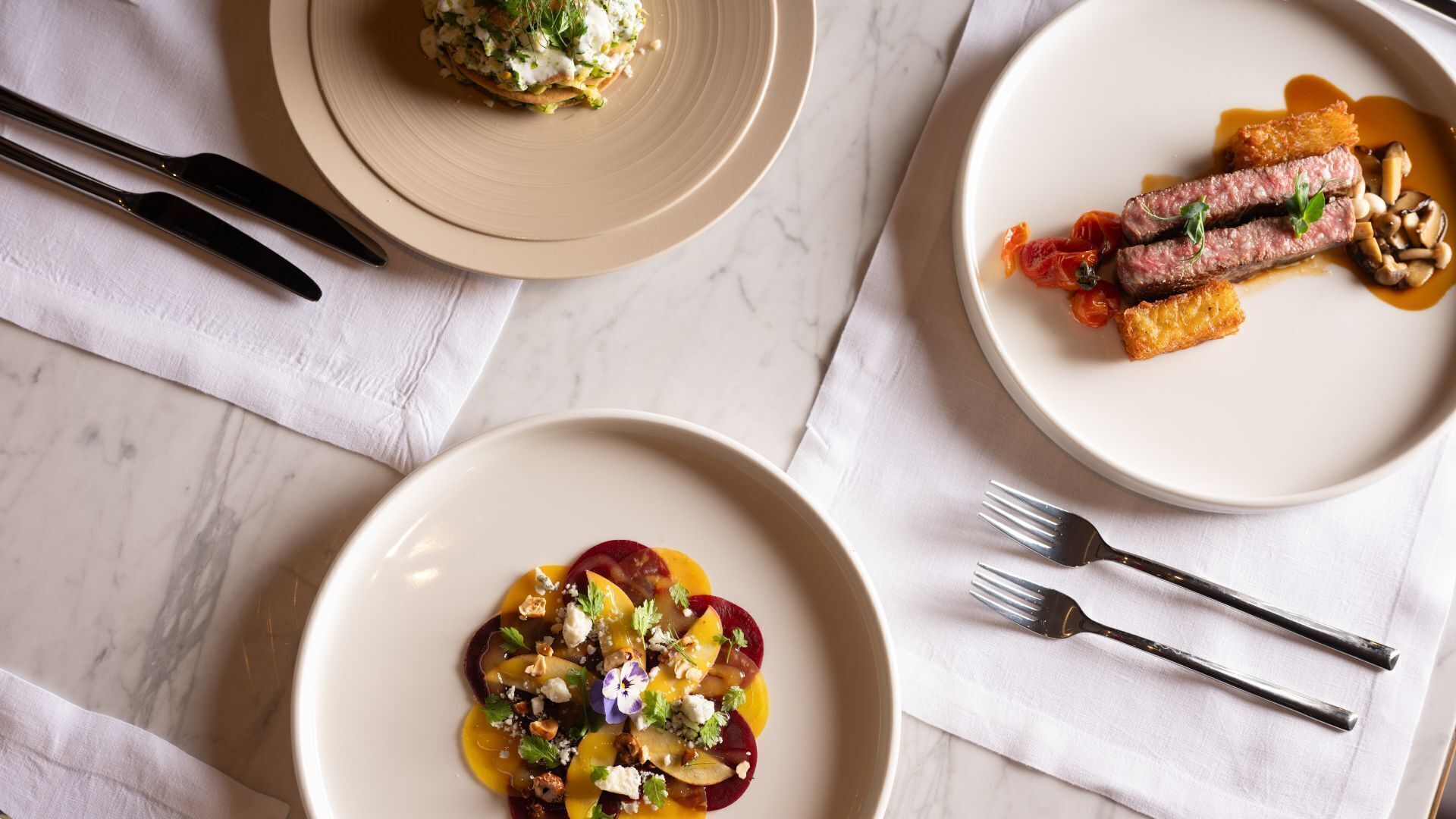 Three plates of food on a marble table with cutlery.