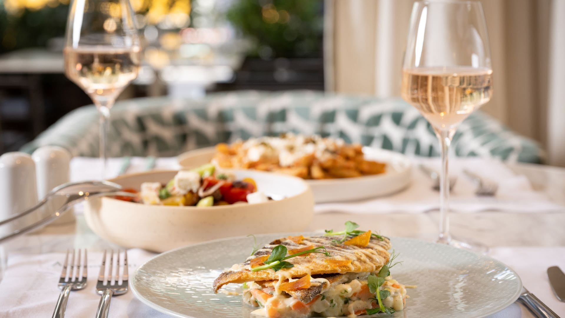 Une table à manger avec une assiette de nourriture, deux verres à vin et une fourchette.