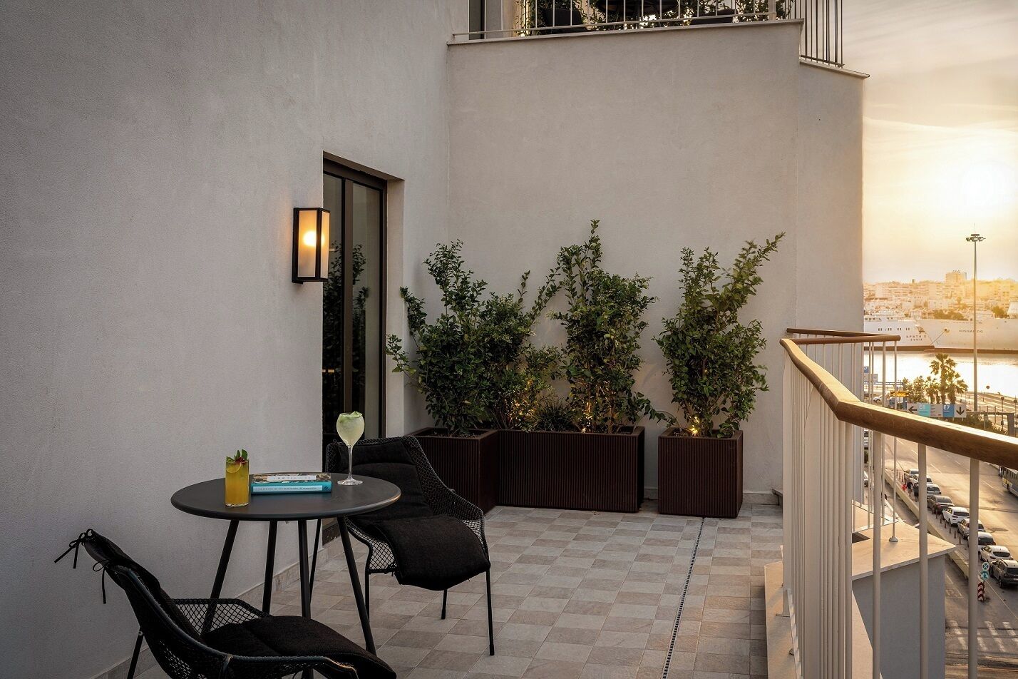 A balcony with a table and chairs, potted plants, and a view of the cityscape.