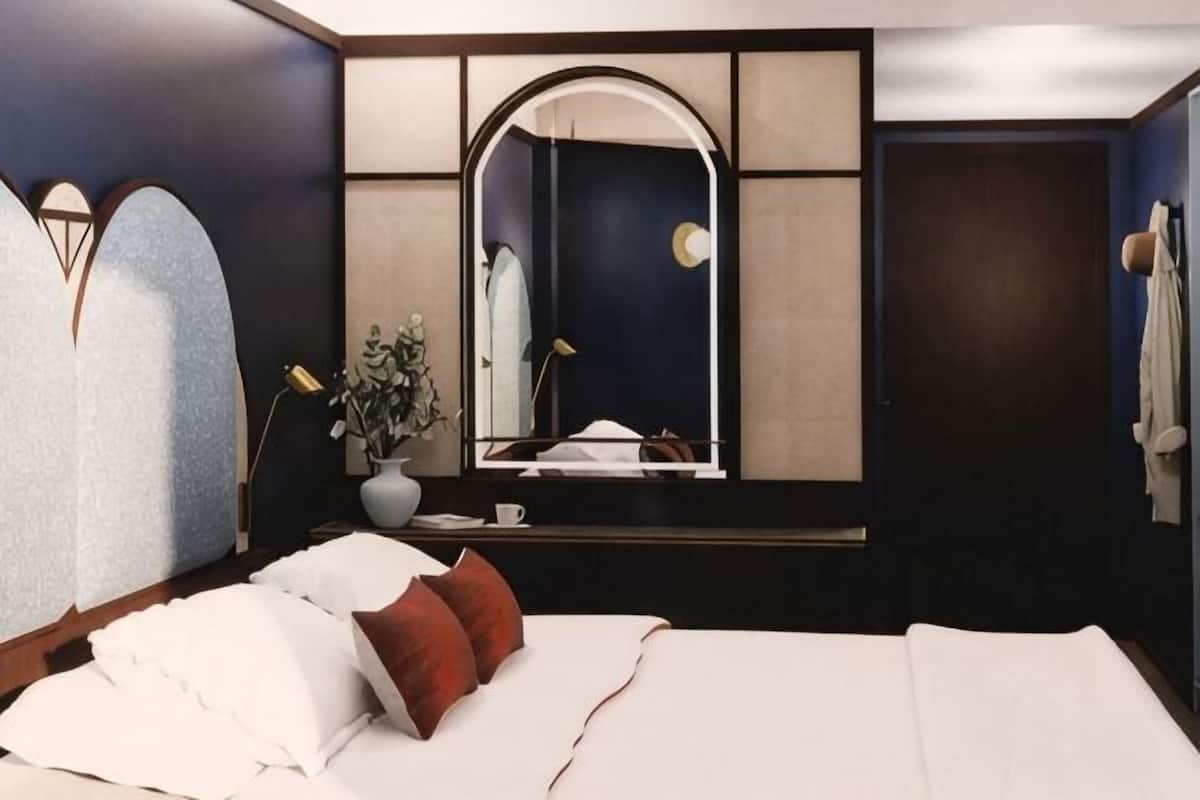 A bedroom with a bed, a mirror, a vase with flowers, and a dark wall.