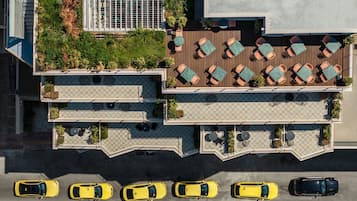 A multi-story hotel with outdoor seating areas, a parking lot, and a green space with plants.