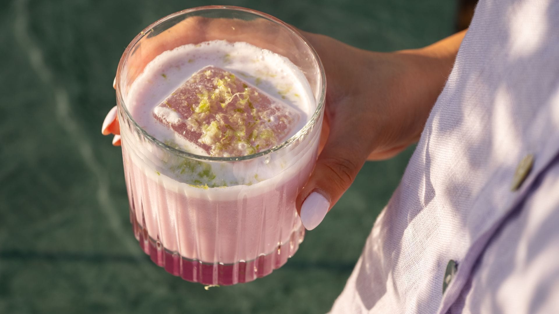 A person holding a glass with a pink beverage and a garnish.