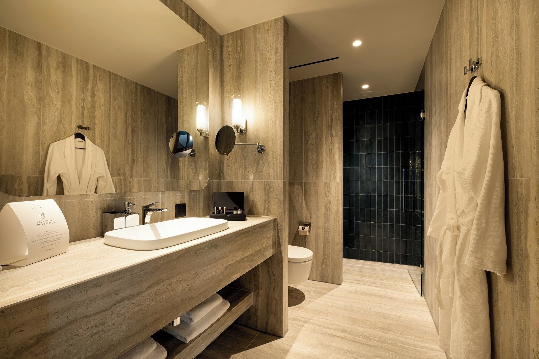 A modern bathroom with a large mirror, two wall-mounted lights, a sink, and a toilet.