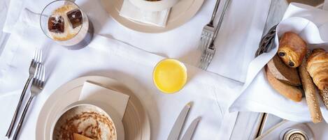 A breakfast setting with a bowl of oatmeal, a glass of orange juice, croissants, and a plate of bread.