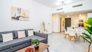 A modern living room with a grey sofa, a wooden coffee table, and a dining area with white chairs and a small table. - Tanin-Beautiful and Modern Apartment with Huge Space (Dubai)