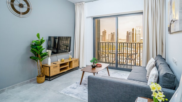 A modern living room with a sofa, TV, and a large window with a city view. - Tanin-Beautiful and Modern Apartment with Huge Space (Dubai)