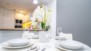A dining table set with white plates, silverware, and wine glasses, with a vase of white orchids in the center. - Tanin-Beautiful and Modern Apartment with Huge Space (Dubai)