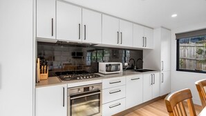 A modern kitchen with white cabinets, stainless steel appliances, and a wooden dining table.
