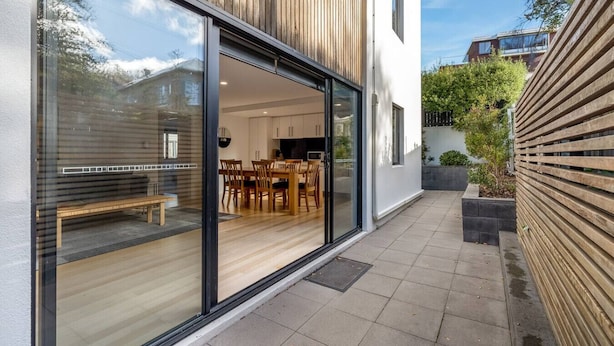 A modern house with a large glass door leading to a dining area with wooden furniture.