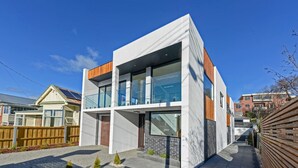 A modern two-story house with a balcony, a wooden fence, and a paved driveway.
