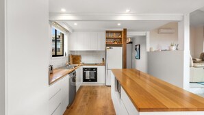 Una cocina moderna con muebles blancos, encimera de madera y electrodomésticos integrados.