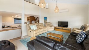 Una sala de estar moderna con un sofá, una mesa de centro y un televisor. Hay una zona de cocina con una ventana y una mesa de comedor.
