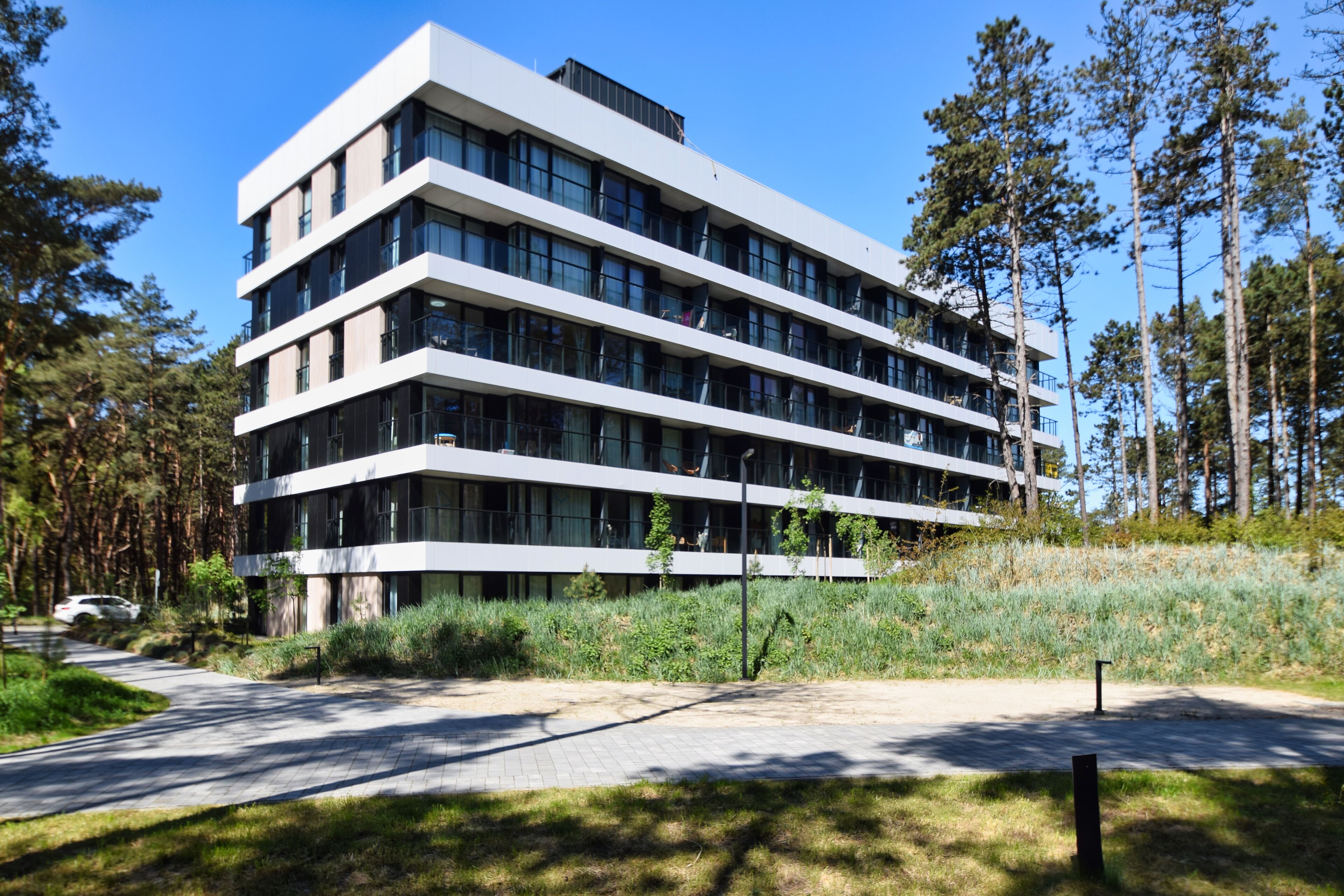 A modern multi-story building with a flat roof, large windows, and a paved pathway leading to it.