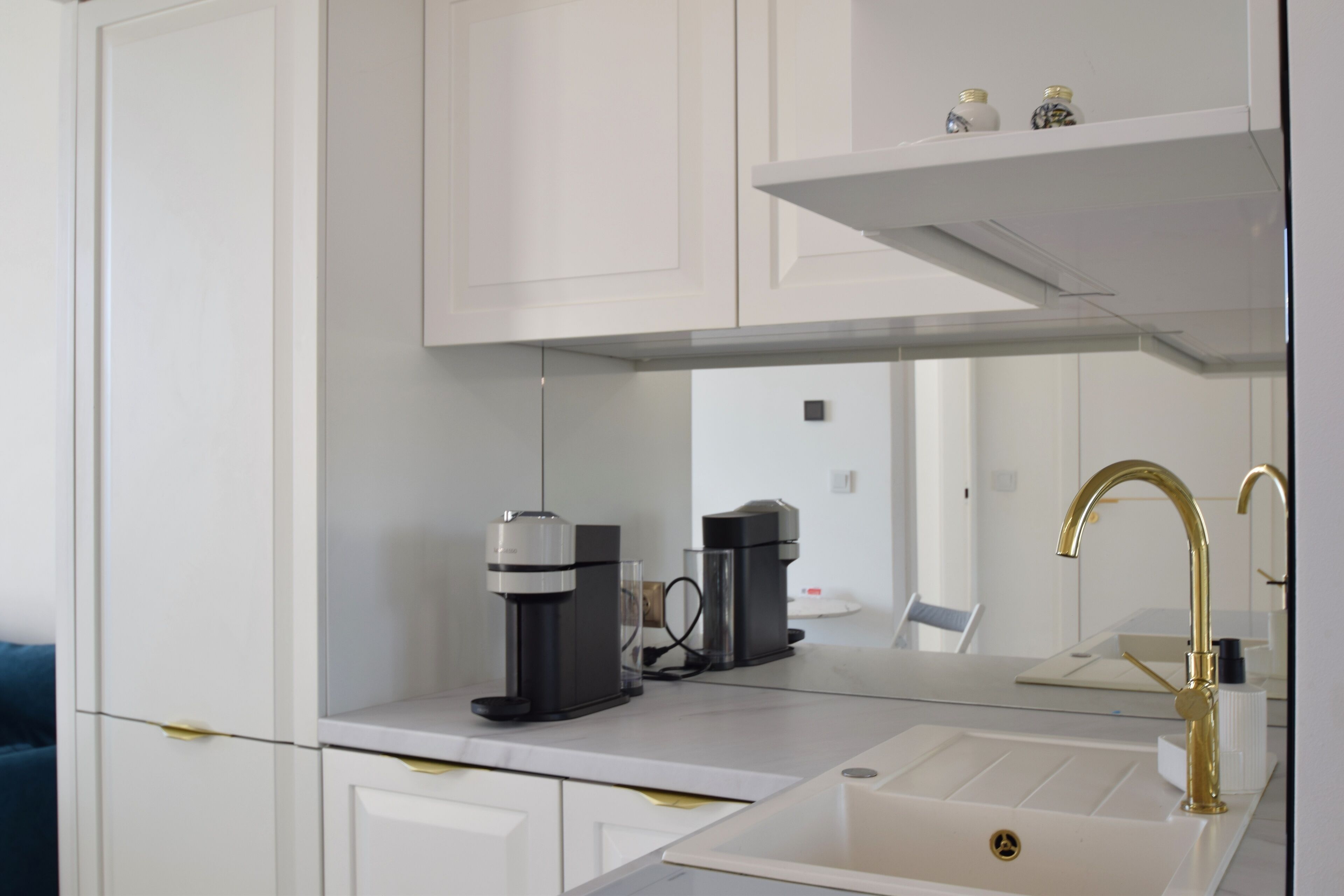 Una cucina moderna con mobili bianchi, una macchina per il caffè e un rubinetto dorato.