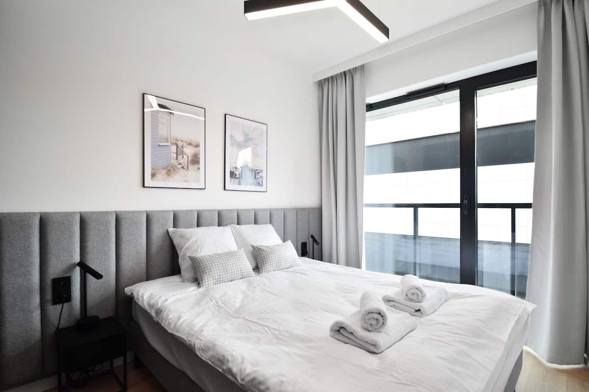 Quarto de hotel moderno com uma cama grande, cabeceira cinzenta e duas imagens emolduradas na parede.