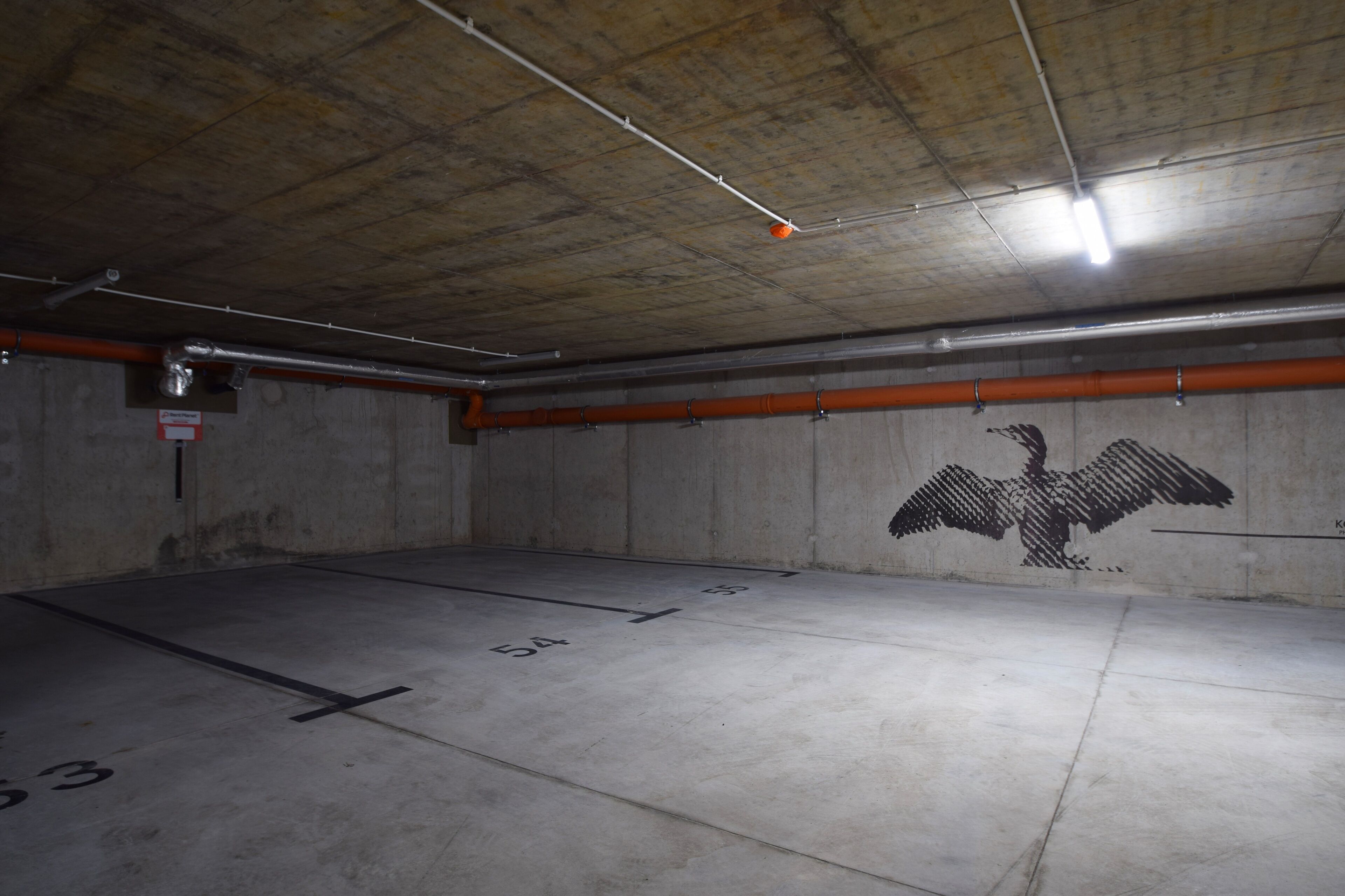 Un parcheggio sotterraneo con pareti in cemento, un murale con un'aquila e posti auto numerati.
