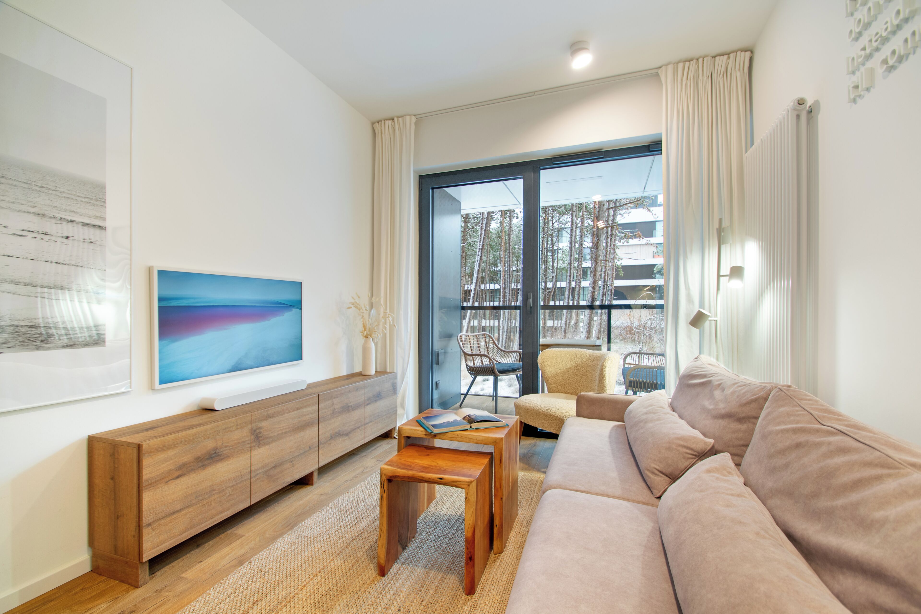 Ein modernes Wohnzimmer mit einer Holzkonsole, einem beigen Sofa und einem großen Fenster mit Blick auf einen Balkon.