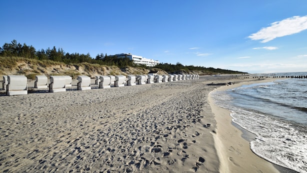 A sandy beach with footprints, a concrete sea wall, and a building in the background. - RentPlanet - Shellter (Trzebiatow)