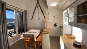 Quarto compacto com cama, uma mesa pequena, cozinha compacta e vista pela janela.