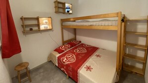 Uma cama beliche com edredom vermelho e branco, um banquinho pequeno, uma prateleira com uma luminária e uma escada.