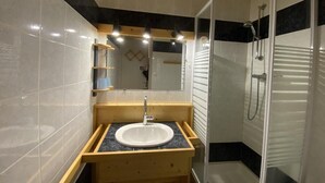 Uma casa de banho moderna com toucador de madeira, lavatório, espelho e cabine de duche.