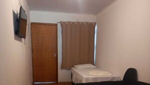 Une petite pièce au mobilier sommaire, avec un plancher en bois, un lit, un bureau et une porte.