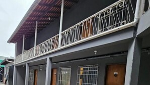 Un bâtiment à l’extérieur gris, doté d’une galerie couverte avec des rampes en métal et d’un sol carrelé.