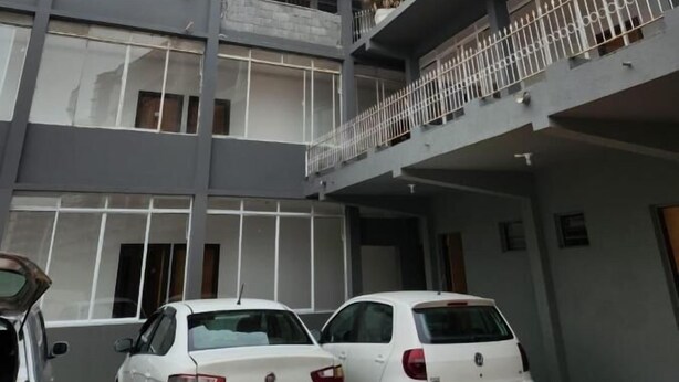 Un immeuble à plusieurs étages, doté d’un toit plat et de balcons. Deux voitures blanches sont garées devant.