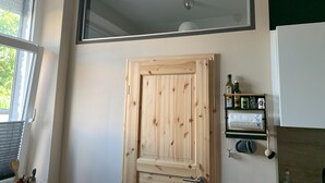 A kitchen with a wooden door, a window with blinds, a ceiling fan, and a shelf with kitchen items.