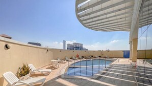 Un espace piscine aménagé sur le toit, avec des chaises longues et une vue dégagée sur les toits de la ville.