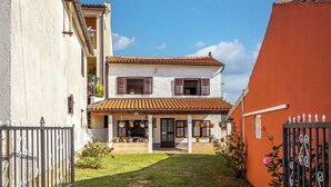 A two-story house with a tiled roof, a front porch with hanging flower baskets, and a small garden area. - Lovely House Luiza (Tar-Vabriga)