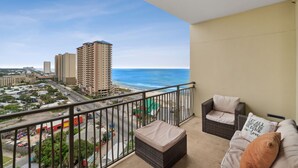A balcony with wicker furniture, a view of the ocean, and high-rise buildings in the background. - Origin 1231 - One Bedroom - Sunrise and Gulf Views (Panama City Beach)