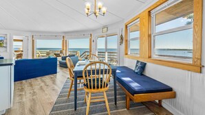Habitación de estilo náutico con comedor, una banca y ventanas amplias con vistas al mar.