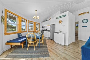 A compact kitchen with white cabinets, a stainless steel refrigerator, and a dining area with a bench and chairs.