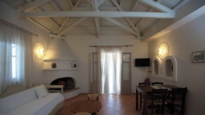A cozy living room with a fireplace, a dining table with chairs, and a television mounted on the wall. - Likavgies Comfort Maisonettes (Alonissos)